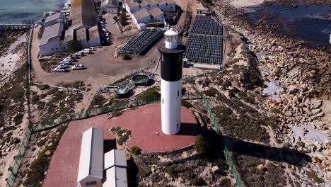 Drone-pullback-reveals-black-and-white-lighthouse-in-Doringbaai,-Weskus