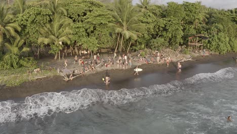 People-bathing-and-surfing-at-Uvita-beach-in-the-Pacific-coastline-during-the-Envision-Festival-gathering,-Aerial-pan-left-reveal-shot