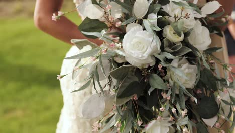 Nahaufnahme-Der-Braut-Und-In-Ihrem-Hochzeitskleid,-Die-Einen-Blumenstrauß-In-Ihren-Händen-Im-Freien-Mit-Weißen-Rosen-Und-Grün-Hält,-1080p-60fps
