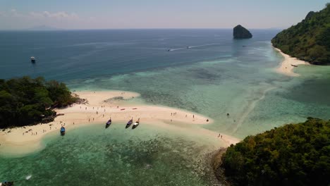 Drone-Aéreo-Sobre-La-Isla-Thale-Waek-En-El-Mar-De-Andaman-De-Krabi-Tailandia-Mientras-Los-Turistas-Llegan-En-Botes-Tailandeses-De-Cola-Larga-Para-Disfrutar-Del-Hermoso-Banco-De-Arena-Y-El-Arrecife-De-Coral-En-Un-Día-Soleado