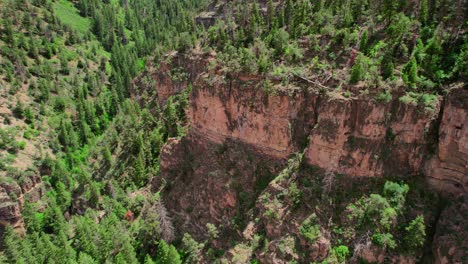 HD-Drone-Shot-Flying-Over-Rocky-Canyon-Cliff-Covered-In-Healthy-Green-Trees-During-Bright-Summer-Day