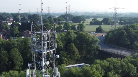 5G-signal-tower-antenna-in-British-countryside-with-vehicles-travelling-on-highway-background-close-up-descending-aerial-view