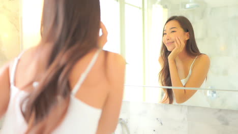 Schöne-Asiatische-Frau,-Die-In-Einen-Spiegel-Schaut-Und-Ihr-Gesicht-Berührt