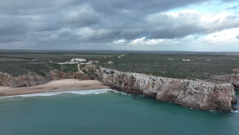 Long-aerial-shot-following-a-coastline-of-beaches-and-cliffs-in-a-rural-area-underneath-a-cloudy-sky