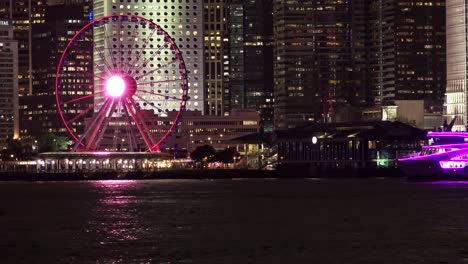 Victoria-Harbour-with-Purple-Ferry-Sailing-by-the-Ferris-Wheel,-Hong-Kong