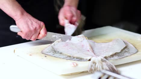 A-fish-vendor-cleans-up-a-nice-monkfish-with-a-kitchen-knife,-over-a-white-cutting-board