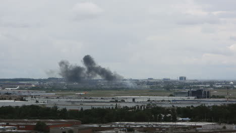 An-aircraft-rolls-down-the-taxiway-as-dark-smoke-billows-from-a-fire-on-tarmac