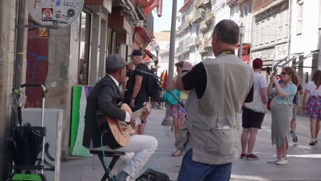 Busker-with-guitar-plays-on-streets-of-Ribeira-with-tourist-taking-photo-in-Historic-Centre-Porto,-Portugal