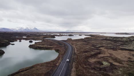 Vista-Aérea-De-Seguimiento-De-Un-Automóvil-Que-Conduce-Cerca-Del-Lago-Myvatn-En-Un-Hermoso-Paisaje-En-Islandia