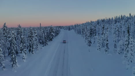 Aerial-view-vehicle-on-journey-through-quiet-snowy-Sweden-woodland-landscape-at-sunset