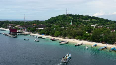 ferry-boat-with-tourists-docking-on-white-sand-beach-at-Gili-Trawangan-Island-in-Bali-Indonesia,-aerial