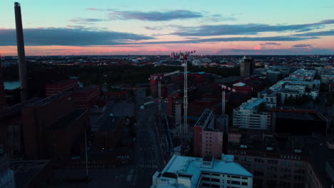 Aerial-view-tilting-towards-construction-cranes-in-Ruoholahti,-dusk-in-Helsinki,-Finland