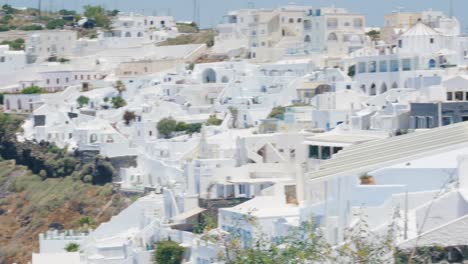 Elder-tourist-couple-walking-together-on-path-near-all-white-buildings-on-cliffs-of-Santorini-Island-hillside-in-Fira,-Greece