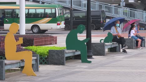 Residents-sit-on-an-outdoor-public-bench-as-they-use-umbrellas-against-weather-conditions-in-Hong-Kong