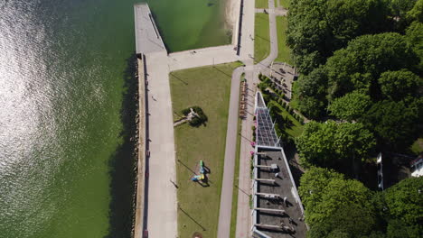 Luftaufnahme-Aus-Der-Vogelperspektive-Von-Spaziergängern-Auf-Der-Promenade-In-Gdingen-Mit-Sonnenreflexion-Im-Wasser