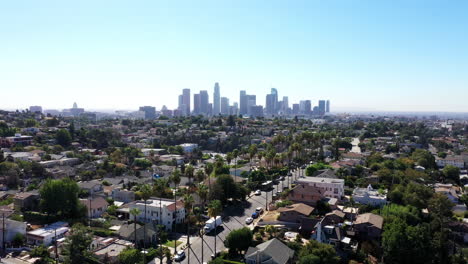 Beautiful-drone-shot-of-Los-Angeles,-California-showing-neighborhoods,-streets,-cars,-mansions,-palm-trees-and-the-city-skyline-against-a-blue-sky-during-golden-hour