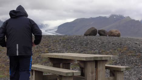 Hombre-Caminando-A-La-Mesa-De-Picnic-Con-Glaciar-En-Segundo-Plano.