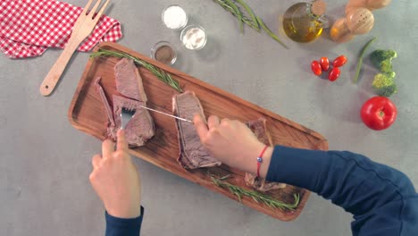 Top-view-static-shot-of-female-hands-cutting-steak-over-wooden-dish