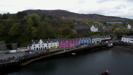 Beautiful-Scottish-Portree-harbour-picturesque-colourful-coastal-vacation-houses-aerial-view-rising-reveal-mountain-scenery