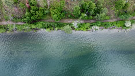 Drone-shot-looking-down-on-a-lake-shoreline-with-trees-and-a-pathway