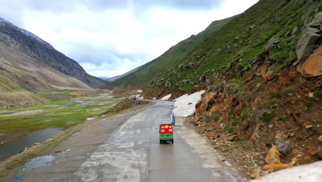 Drone-shot-following-a-tuk-tuk-on-the-Babusar-Pass-mountain-pass-in-Pakistan,-in-the-Kaghan-Valley