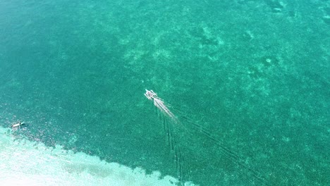A-traditional-outrigger-fishing-canoe-boat-with-a-motor-moving-through-crystal-clear-turquoise-ocean-water-above-coral-reef-on-a-remote-tropical-island,-aerial-drone