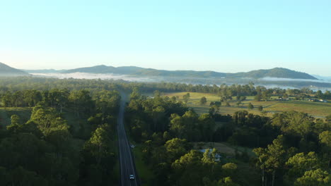 Drone-4K-Aerial-Above-Rural-Road-In-Green-Australian-Hinterland-Landscape-With-Fog-On-Horizon