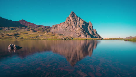 Timelapse-of-Anayet-peak-and-blue-tent-near-lake-reflection-in-Pyrenees-mountains-during-a-full-moon-night,-Aragon,-Spain
