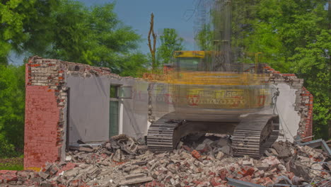 Static-shot-of-concrete-house-been-broken-down-by-bulldozer-in-timelapse-using-mechanical-arm-with-green-vegetation-at-daytime