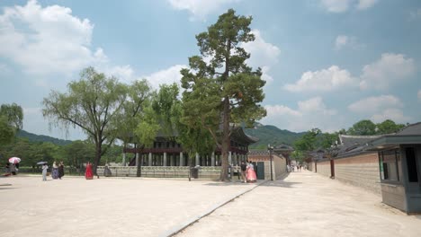 Reisende-In-Traditionellen-Hanbok-Kostümen-In-Der-Nähe-Des-Gyeonghoeru-Pavillons-Im-Gyeongbokgung-Palast-An-Einem-Sommertag-–-Weite-Aussicht-Mit-Weißen-Wolken,-Die-Am-Blauen-Himmel-Schweben