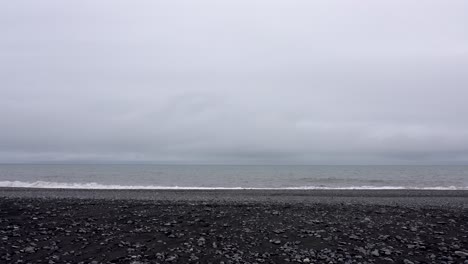 Static-shot-of-black-sand-beach-and-dark-cloudy-sky-on-Iceland---Waves-reaching-shoreline-during-misty-day