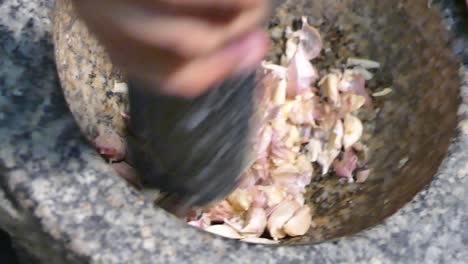 Asian-Hand-Using-Stone-Mortar-and-Pestle-Crushing-Garlic,-Close-Up,-Slow-Motion