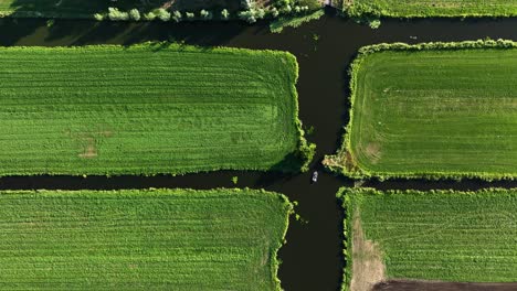 Top-down-view-of-motorboat-glide-in-dark-polder-farmland-canal-by-field