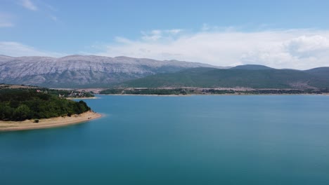 Frente-Al-Azul-Profundo-Del-Lago-Croata-Perucko-Con-Una-Playa-Brillante,-Detrás-De-Las-Imponentes-Montañas-Dinara-En-Un-Clima-Agradable-Y-Soleado