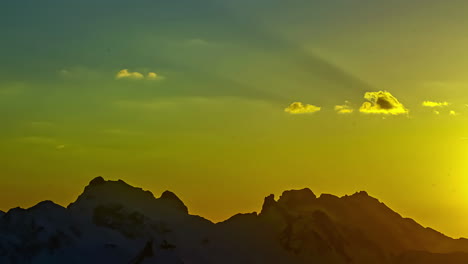 The-rugged-snowy-peaks-of-the-European-Alps-mountain-range-during-a-bright-sunset---time-lapse