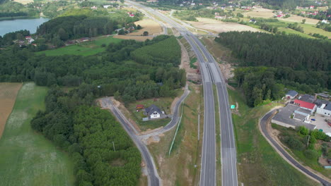 Ascending-aerial-shot-of-empty-highway-in-rural-area-of-Poland-with-forest-trees-and-lake
