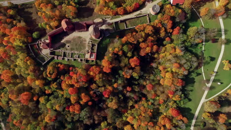 Aerial-drone-bird's-eye-view-over-old-Turaida-Castle-surrounded-by-colorful-autumnal-forest-landscape-during-evening-time