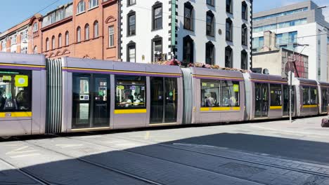 The-Dublin-tram-going-along-Abbey-Street,-with-many-people-walking-through-the-streets-on-a-sunny-day