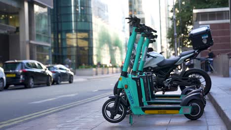 London-Canary-Wharf-Aug-2022-row-of-electric-scooters-and-bike-parked-by-the-side-of-the-road-waiting-for-passengers
