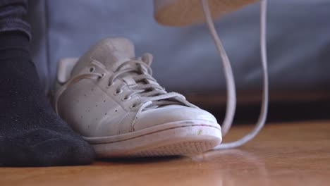 Close-up-of-male-putting-on-white-sneakers-on-black-socks-and-tying-shoelaces