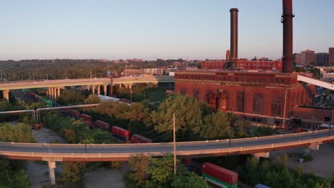 Aerial-descending-close-up-shot-of-a-brick-factory-with-a-passing-freight-train-in-Kansas-City,-Missouri-at-sunset