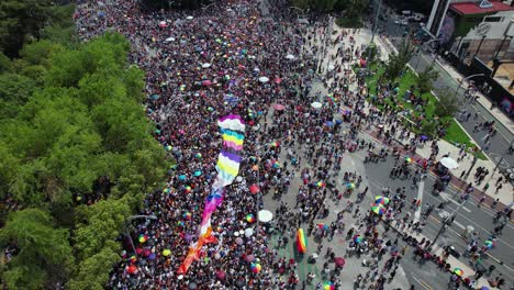Aerial-view-over-people-carrying-a-flag,-on-Avenida-Paseo-de-la-Reforma-at-the-Gay-Pride-Parade-in-Mexico-city---tilt,-drone-shot