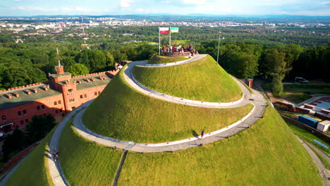 Kościuszko-Mound-Poland,-Hill-of-Kościuszko,-Panoramic-Aerial-View-of-Artificial-Mound-Historical-Exhibits-Monument-in-Kraków,-Tourists-Visiting-Serpentine-Path-Leads-to-the-Top,-Cityscape-in-Horizon