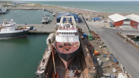 An-aerial-view-from-the-forward,-fishing-trawler-lifted-out-of-water-in-a-dry-dock-for-repair-and-painting-work-in-Hanstholm