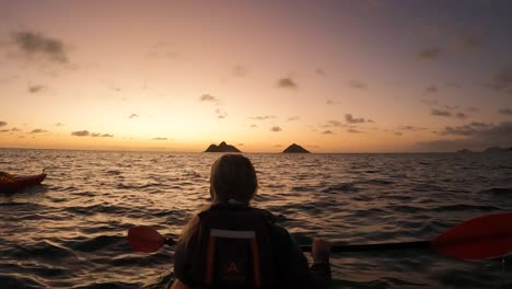 Rear-view-of-young-woman-kayaking-on-sea-towards-sunset,-slow-motion