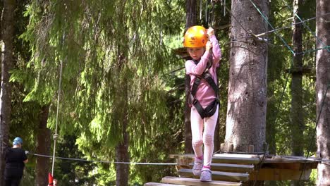 Cute-6-year-old-girl-with-helmet-and-safety-harness-facing-her-fears-when-climbing-inside-Voss-zipline-and-climbing-park---Norway-sunny-day-slow-motion