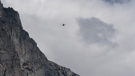 Drone-dji-mini-3-pro-hovering-in-the-air-and-it-does-not-move,-detached-from-the-cloudy-sky-and-near-a-rocky-mountain-peak,-Switzerland