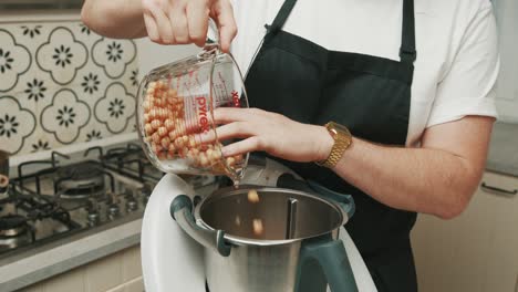 Chef-pouring-chickpeas-in-blender-for-hummus-preparation-process