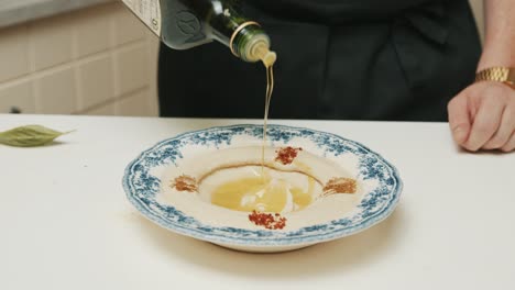 Koch-Gießt-Olivenöl-Auf-Frisch-Zubereiteten-Hummusteller