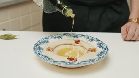 Chef-pouring-olive-oil-on-freshly-made-hummus-plate